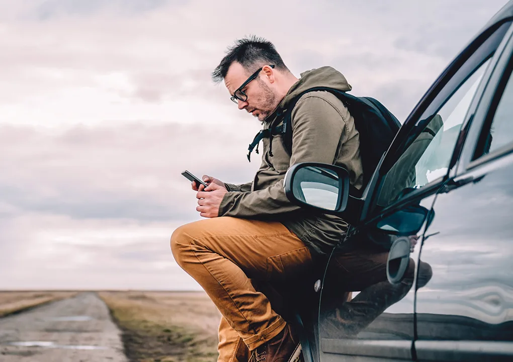 A man sat on a car looking at phone