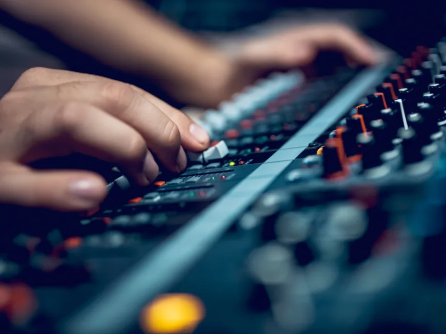 Hands pushing faders on mixing desk.