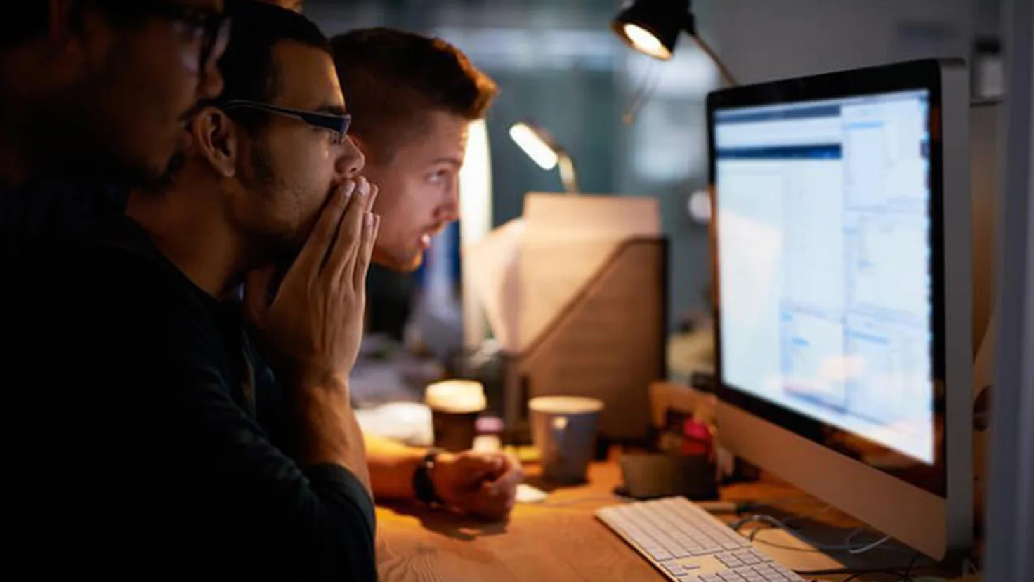 Three men looking at computer screen at office desk